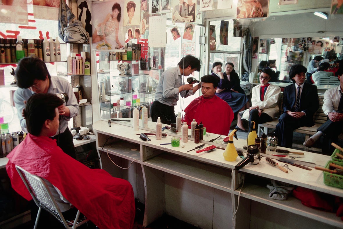1989年一間髮廊裏，髮型師細心用風筒為顧客吹起「飛機頭」。髮廊生意很好，鏡子展示後排坐滿輪候理髮的客人。