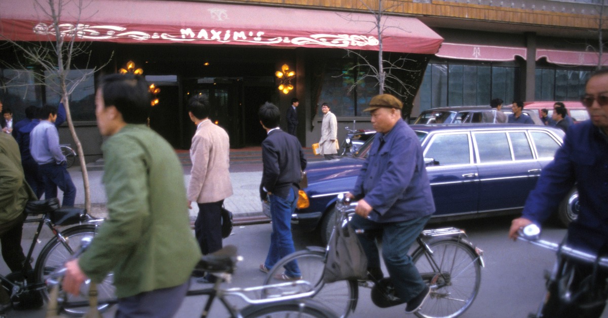 圖為1985年北京。此時全國第一間西餐廳、馬克西姆餐廳（Ｍaxim's）已開業兩年。在北京街頭上，部分人脫去藍綠色的制服，換上個性化的西裝襯衣，他們經過時，不自覺偷望餐廳幾眼。