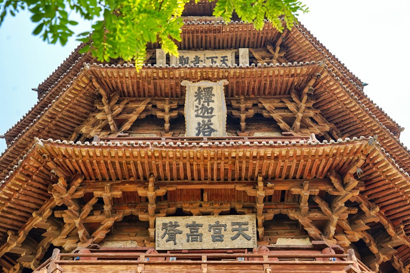 An upward view of the facade of the Yingxian Wooden Pagoda in Shanxi, showing the multi-layered eaves galleries and complex dougong structures of the Liao dynasty wooden pagoda architecture, with plaques inscribed with 