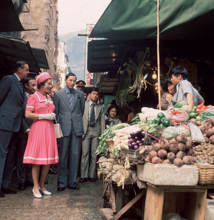 1975年英女王伊利沙伯二世在港督麥理浩（左一）陪同下，到了中環嘉咸街街市與檔主對話。（圖片來源：Getty）　