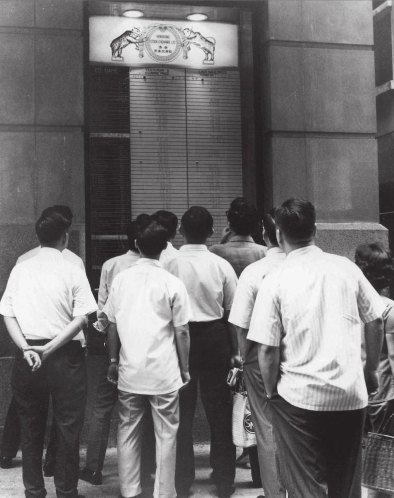 1960年代股民在中環雪廠街公爵行的「香港會」門口，緊貼股市行情。（圖片來源：《香港金融史1841-2017》））