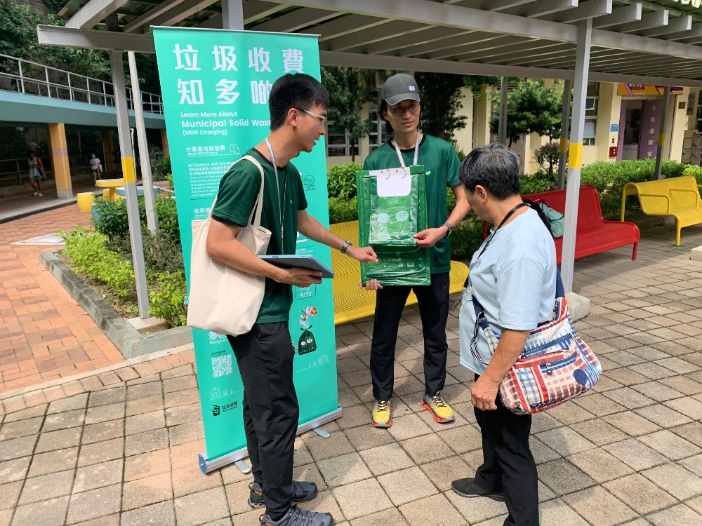 由環保署職員組成的外展隊伍「綠展隊」，向一名居民介紹垃圾收費資料。（圖片來源：政府新聞處）