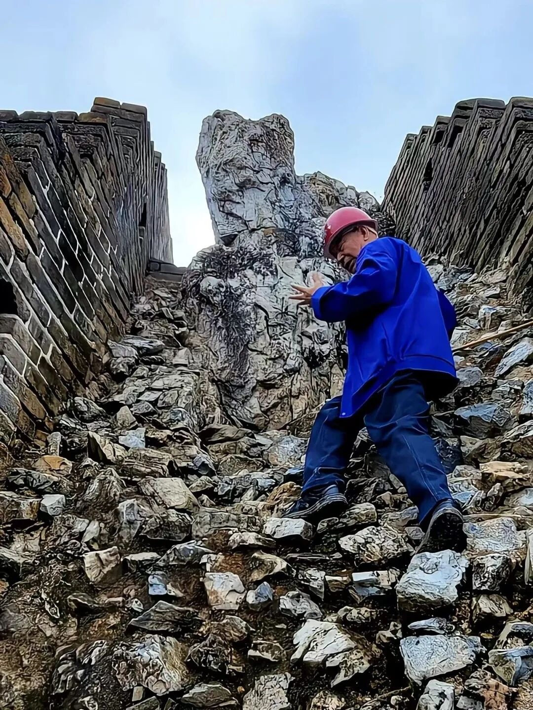 程永茂頭戴紅色安全帽、胸前掛着相機、手持登山杖，遇到陡坡和斷崖，要手腳並用攀爬。