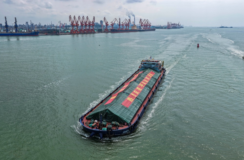廣西欽州港外海航拍圖，一艘載貨船駛離碼頭，背景可見港區起重機、泊位及沿岸工業設施。