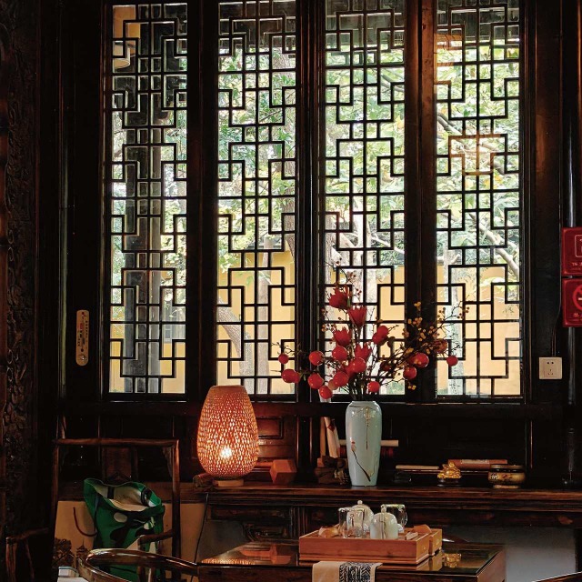蘇州北寺塔茶室，中式木質花窗透進暖光，案上有青瓷紅果、竹編燈籠和茶席。