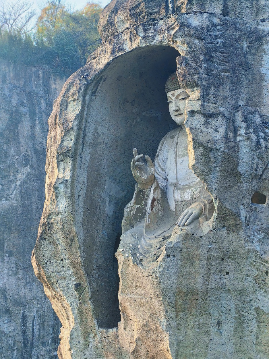 The eyes of the Shaoxing Keyan Giant Buddha are slightly open, gazing somewhat downwards, its ears are close to its shoulders, its countenance is benevolent, its left hand rests on its knee, its right hand is in a gesture of expounding the sutras, and it wears a kasaya in the style of loose robes with a wide sash.