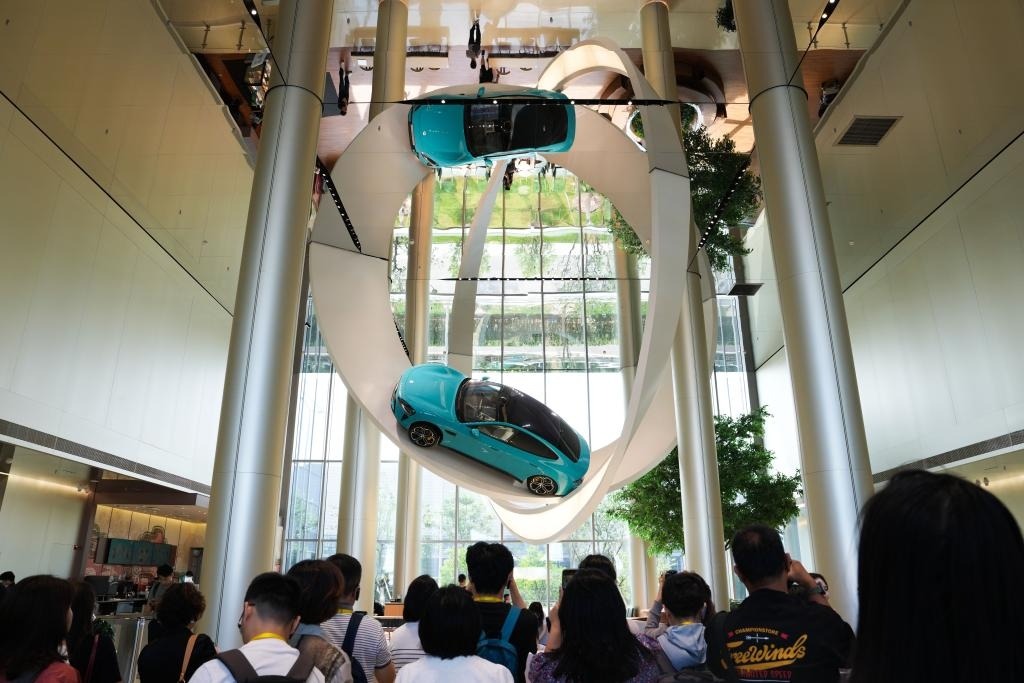 在北京小米汽車超級工廠，展示大廳上空懸掛小米新能源汽車，一群學生在參觀。
