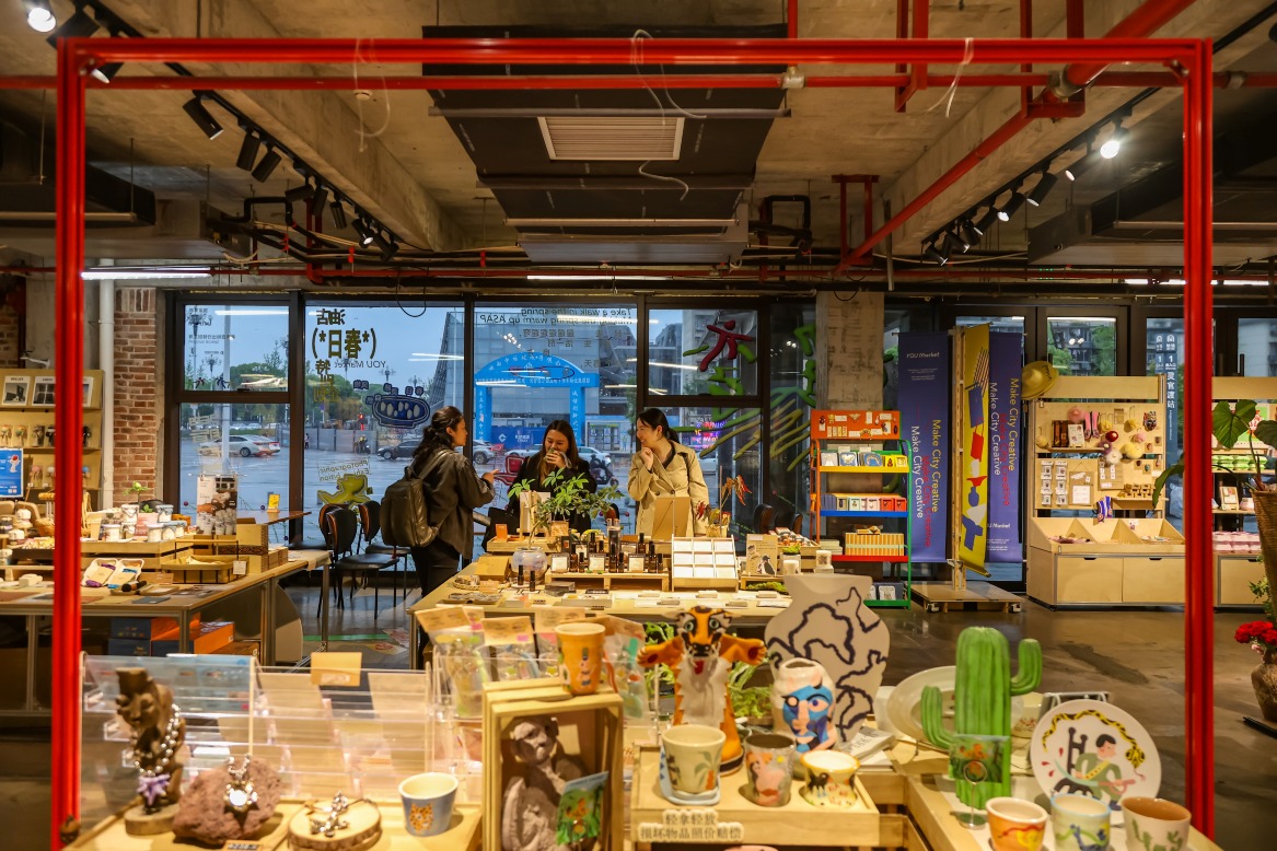長沙城發油脂廠1936文創園一間藝術商店內，陳列陶瓷杯、飾物、擺設及其他文創商品；三名訪客站在店內交談，空間保留紅色管道和工業風天花設計。