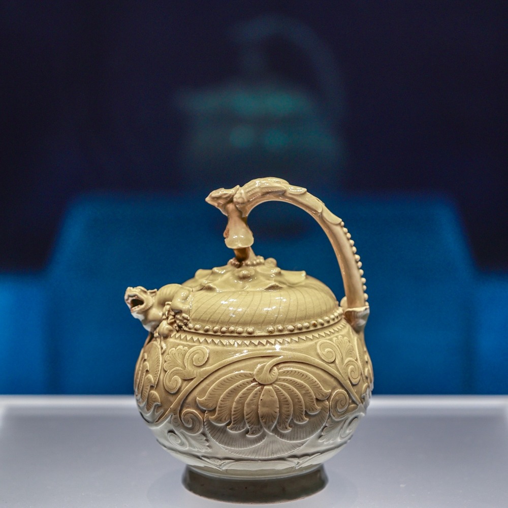 陝西歷史博物館的文物，五代青瓷提梁倒灌壺，瓷壺有伏鳳式提梁，以花蒂象徵壺蓋，蓋、壺銜接處堆塑哺乳母子獅，球形壺腹刻飾纏枝牡丹，造型奇巧，是耀窯瓷器出類拔萃的珍品。