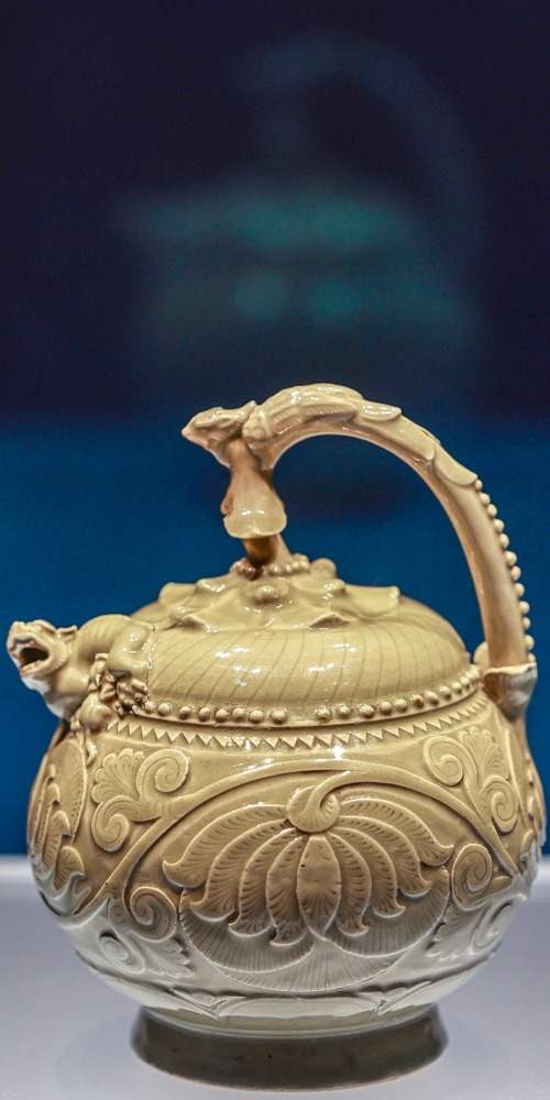 陝西歷史博物館的文物，五代青瓷提梁倒灌壺，瓷壺有伏鳳式提梁，以花蒂象徵壺蓋，蓋、壺銜接處堆塑哺乳母子獅，球形壺腹刻飾纏枝牡丹，造型奇巧，是耀窯瓷器出類拔萃的珍品。