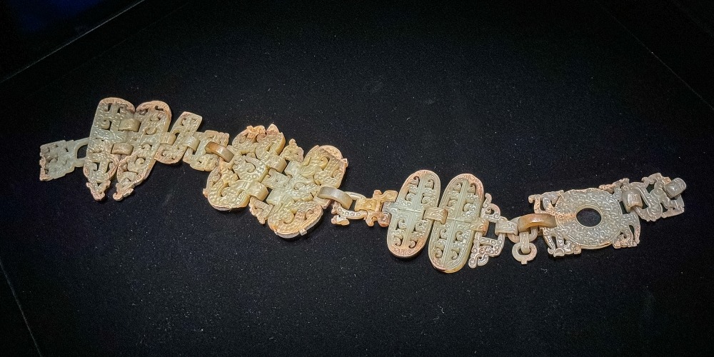湖北省博物館藏戰國早期十六節龍鳳玉掛飾全貌，青白色玉器由多節鏤雕龍鳳紋玉件相連，陳列於黑色展台上。