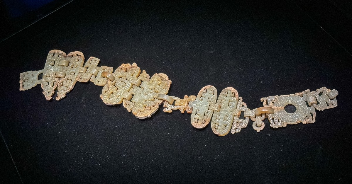 湖北省博物館藏戰國早期十六節龍鳳玉掛飾全貌，青白色玉器由多節鏤雕龍鳳紋玉件相連，陳列於黑色展台上。