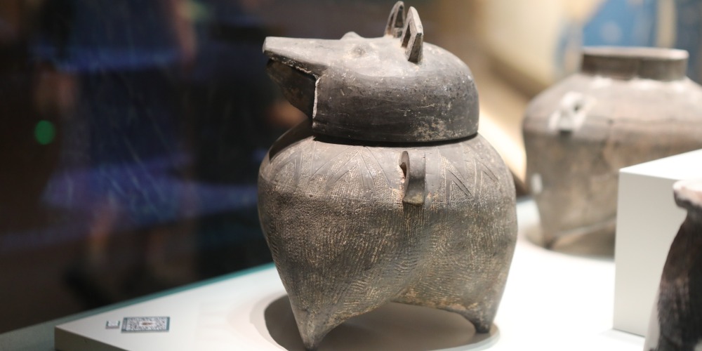 殷墟博物館的文物陶鬲形豬首蓋盉，長嘴、雙耳直立，器身飾繩紋，底部有三隻袋足。