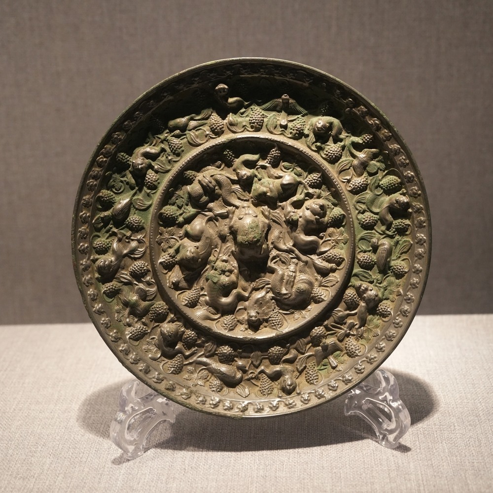 河南洛陽博物館藏唐代海獸葡萄紋銅鏡，鏡背飾瑞獸、葡萄藤蔓、果串及禽鳥紋樣。