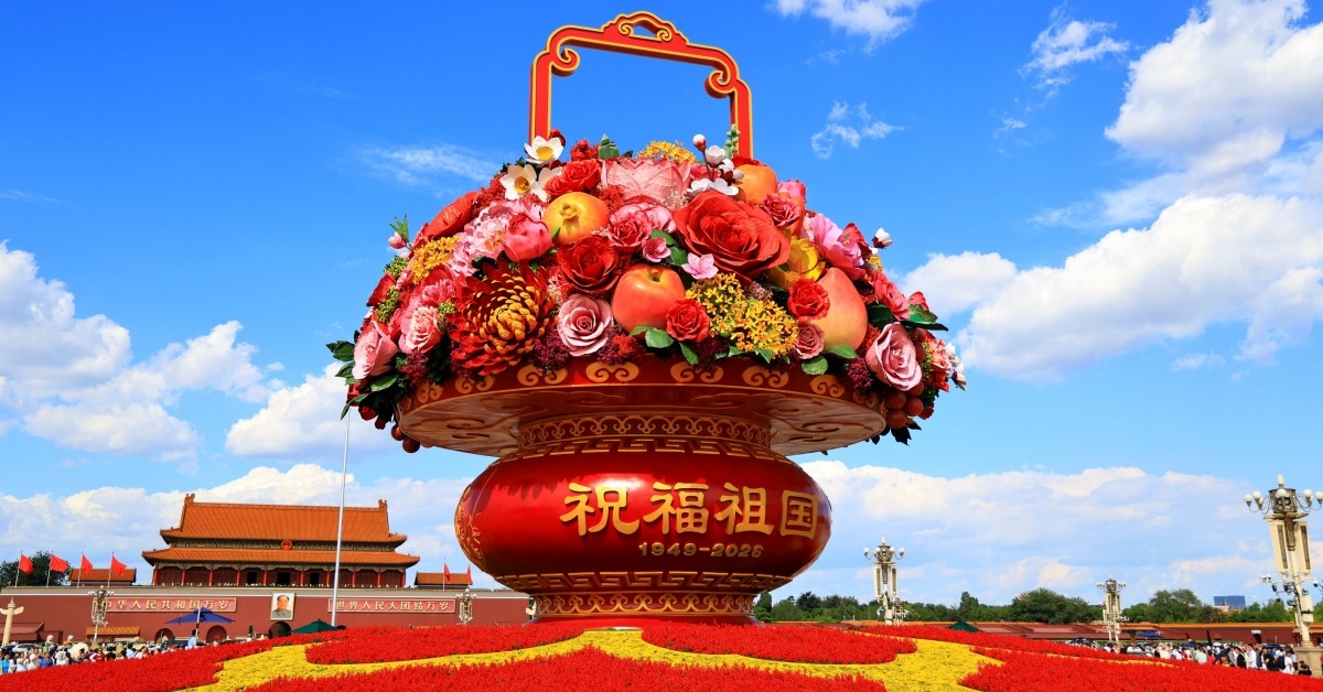 天安門廣場「祝福祖國」巨型花果籃全景，籃身寫有「祝福祖國，1949-2026」，前景為國慶花壇，背景可見天安門城樓與藍天白雲。