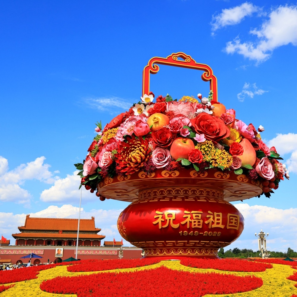 天安門廣場「祝福祖國」巨型花果籃全景，籃身寫有「祝福祖國，1949-2026」，前景為國慶花壇，背景可見天安門城樓與藍天白雲。